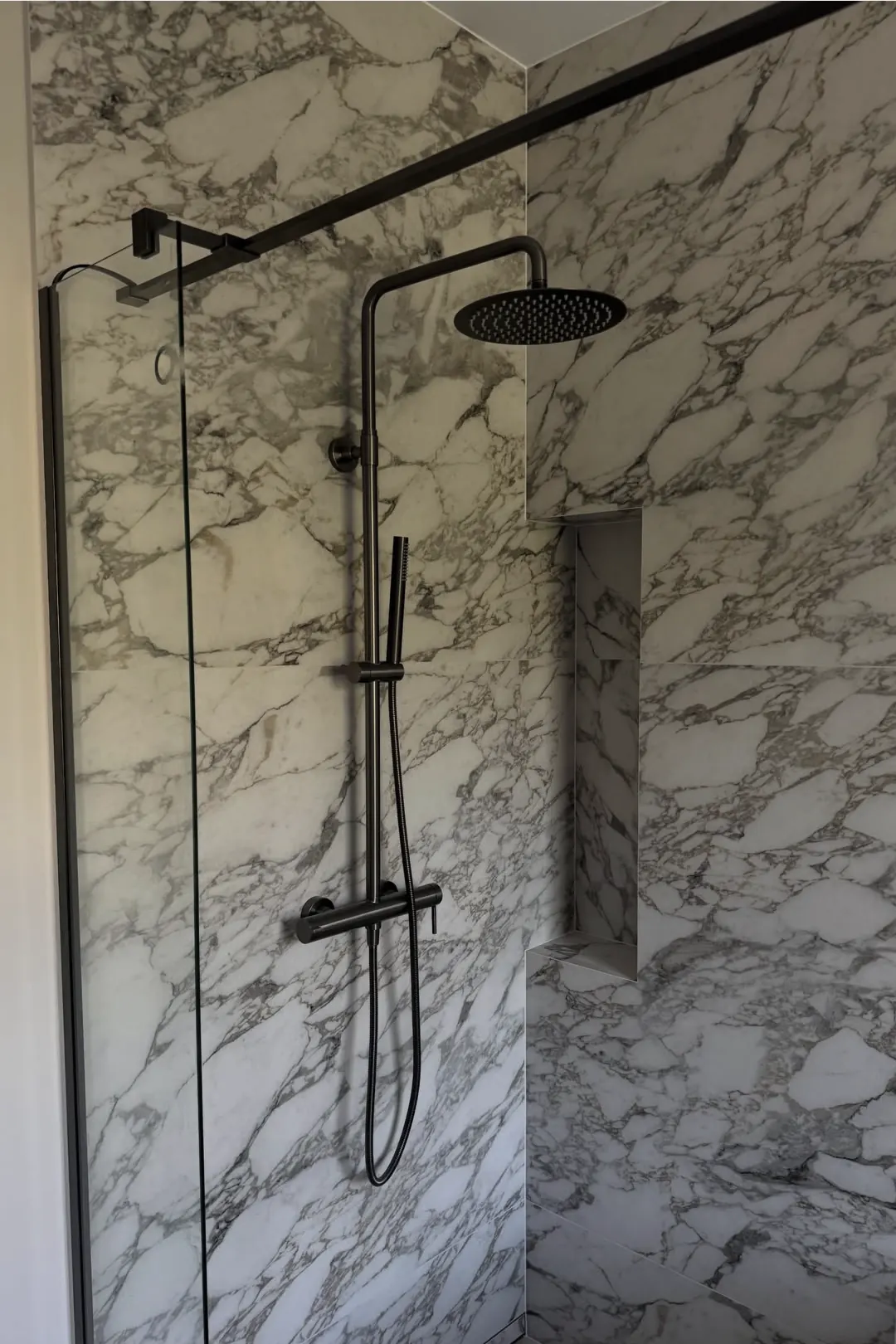 Prysznic walk-in z płyt imitujących marmur, z czarną deszczownicą i wnęką w ścianie